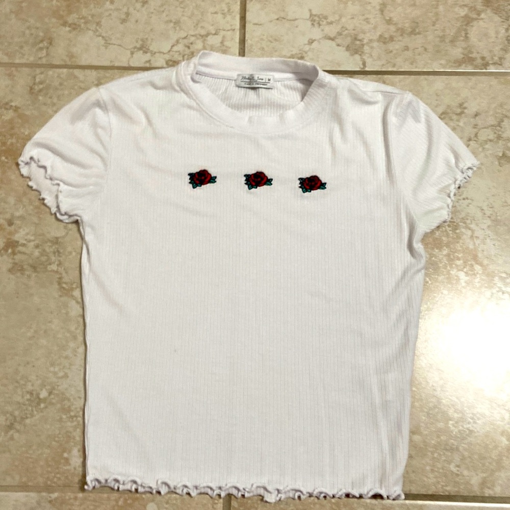 White top with three roses at the top and ruffles at the bottom and sleeves